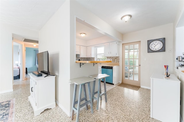 kitchen with a breakfast bar area, dishwasher, kitchen peninsula, decorative backsplash, and white cabinets