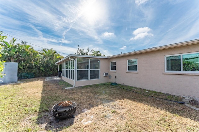 rear view of property with a sunroom, a lawn, and a fire pit