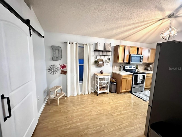 kitchen with hanging light fixtures, light wood-type flooring, stainless steel appliances, a barn door, and backsplash