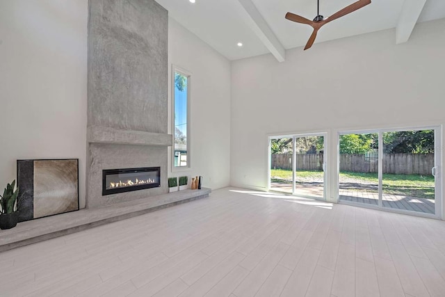 unfurnished living room featuring a high ceiling, ceiling fan, a fireplace, and beam ceiling