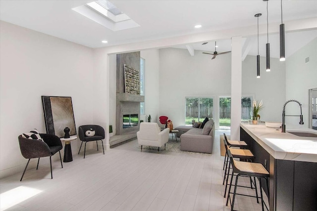 living room with high vaulted ceiling, a fireplace, beamed ceiling, a skylight, and sink