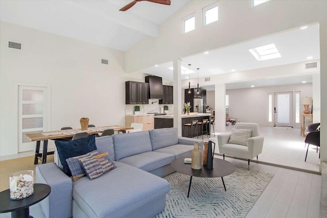 living room with ceiling fan, beam ceiling, high vaulted ceiling, and light wood-type flooring