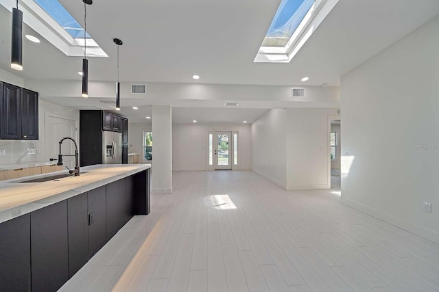 kitchen with a skylight, stainless steel fridge with ice dispenser, sink, and hanging light fixtures