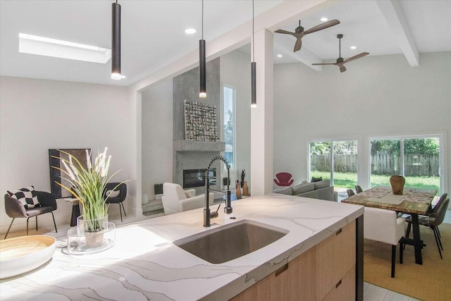 kitchen with sink, a large fireplace, hanging light fixtures, light stone counters, and beam ceiling