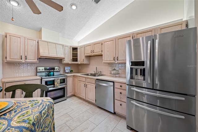 kitchen featuring appliances with stainless steel finishes, tasteful backsplash, lofted ceiling, sink, and light brown cabinets