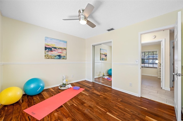 workout room with ceiling fan, dark wood-type flooring, and a textured ceiling