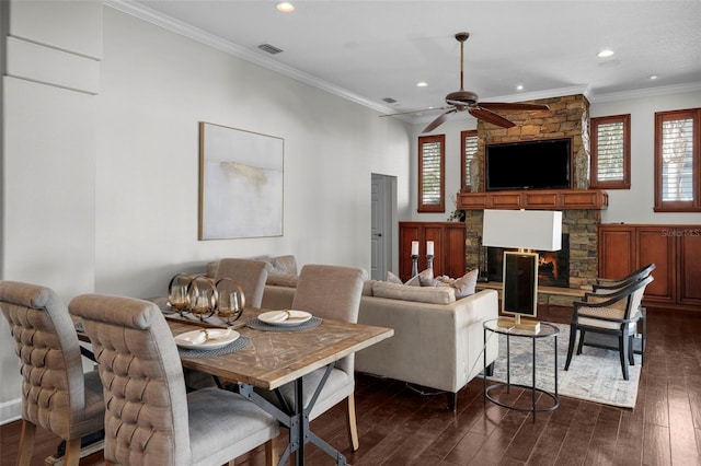 living room with crown molding, ceiling fan, dark hardwood / wood-style flooring, and a stone fireplace