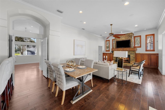 dining space with crown molding, a stone fireplace, dark hardwood / wood-style floors, and ceiling fan