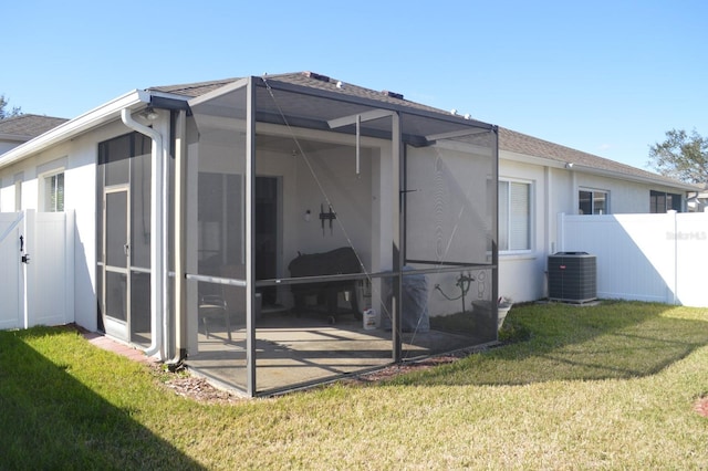 back of property with central AC unit, glass enclosure, and a lawn