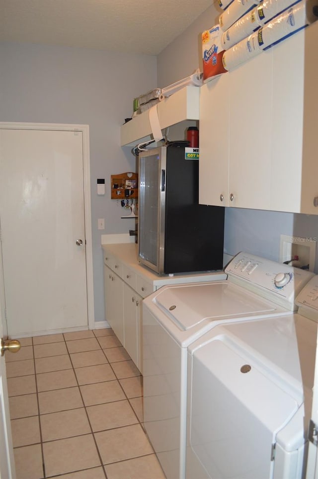 clothes washing area featuring washer and clothes dryer, cabinets, and light tile patterned flooring