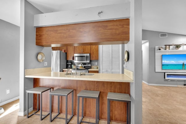 kitchen with vaulted ceiling, appliances with stainless steel finishes, sink, a kitchen breakfast bar, and kitchen peninsula