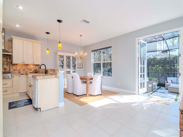 kitchen with tasteful backsplash, wall chimney range hood, decorative light fixtures, and plenty of natural light