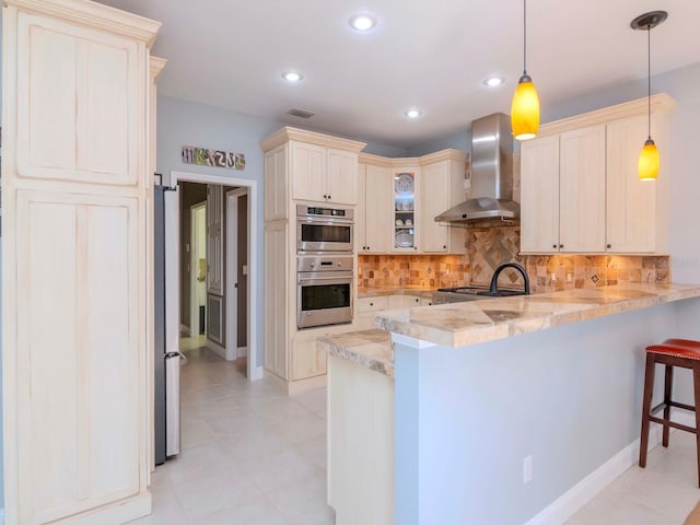 kitchen with a breakfast bar, pendant lighting, double oven, kitchen peninsula, and wall chimney range hood