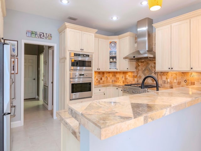 kitchen with wall chimney exhaust hood, range, kitchen peninsula, white fridge, and stainless steel double oven