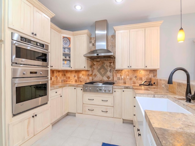 kitchen featuring wall chimney range hood, sink, backsplash, hanging light fixtures, and stainless steel appliances