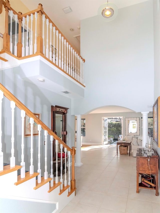 staircase featuring a high ceiling, tile patterned flooring, and decorative columns