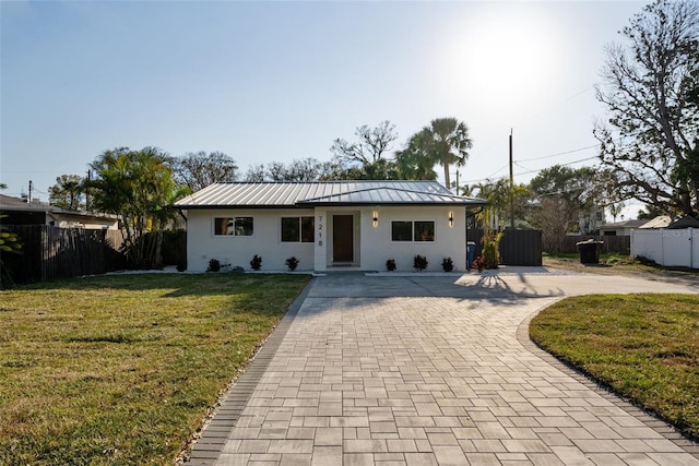 single story home with metal roof, fence, a front lawn, and decorative driveway