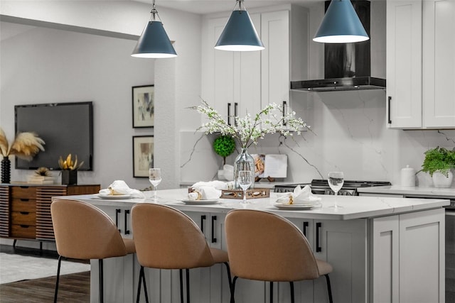 kitchen featuring dark wood-style floors, wall chimney exhaust hood, decorative light fixtures, white cabinetry, and backsplash