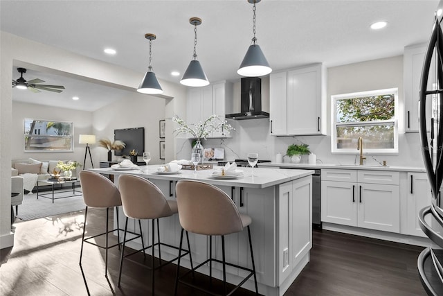 kitchen featuring dark wood-style flooring, white cabinets, a sink, and wall chimney range hood