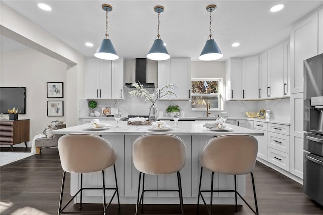 kitchen with dark wood-style floors, a breakfast bar, white cabinetry, a sink, and wall chimney exhaust hood