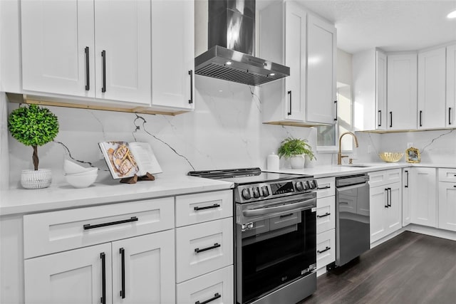 kitchen featuring appliances with stainless steel finishes, white cabinets, a sink, and wall chimney range hood