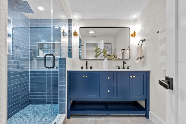 full bathroom featuring double vanity, a shower stall, a sink, and a textured wall