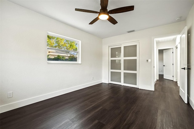 empty room with dark wood-style floors, visible vents, baseboards, and a ceiling fan