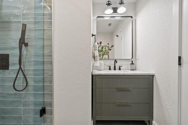 bathroom with visible vents, a textured wall, a tile shower, and vanity