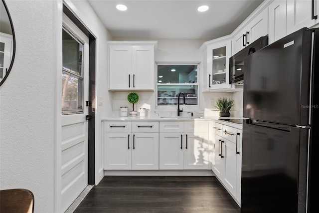 kitchen featuring dark wood finished floors, white cabinetry, a sink, and black appliances