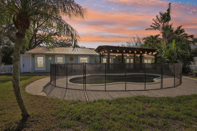 back house at dusk with a fenced in pool and a yard