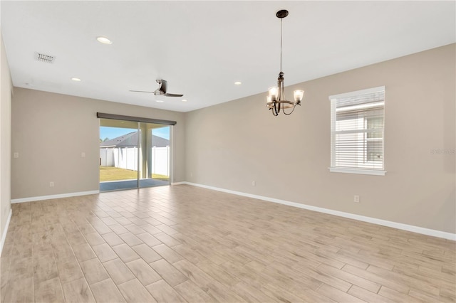 spare room featuring ceiling fan with notable chandelier