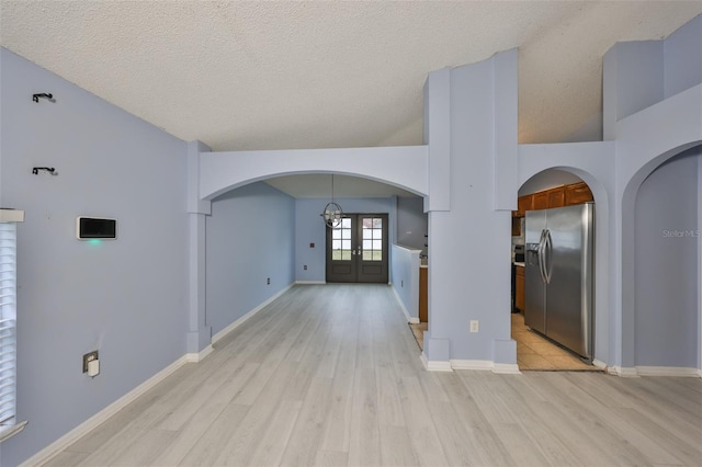 interior space with french doors, a towering ceiling, light hardwood / wood-style floors, and a textured ceiling