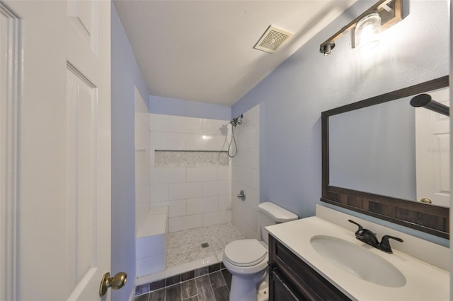 bathroom with tiled shower, vanity, and toilet