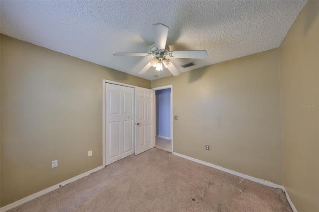 unfurnished bedroom with a textured ceiling, light colored carpet, a closet, and ceiling fan