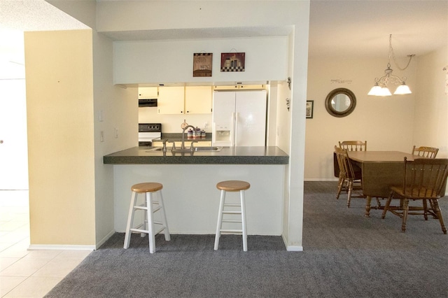 kitchen featuring sink, hanging light fixtures, a kitchen breakfast bar, white fridge with ice dispenser, and white cabinets