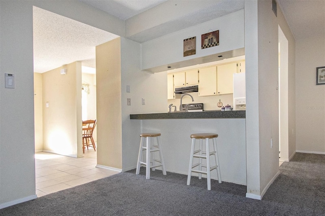 kitchen with a kitchen bar, stainless steel range with electric cooktop, white cabinetry, light tile patterned floors, and kitchen peninsula