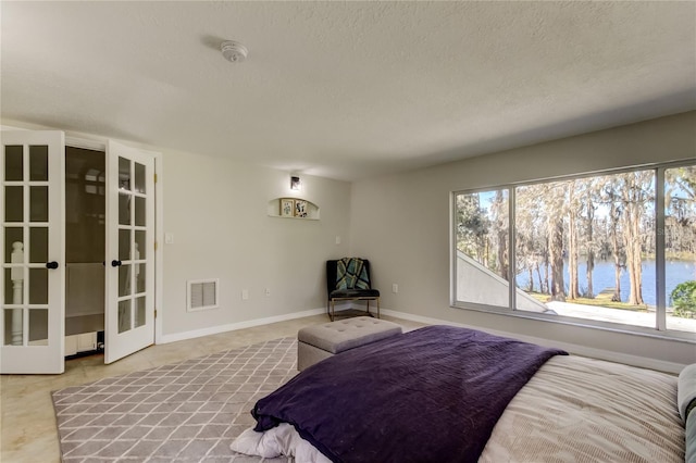 bedroom with a water view, multiple windows, french doors, and a textured ceiling