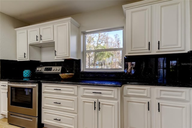 kitchen with dark stone countertops, stainless steel electric range oven, white cabinetry, and tasteful backsplash