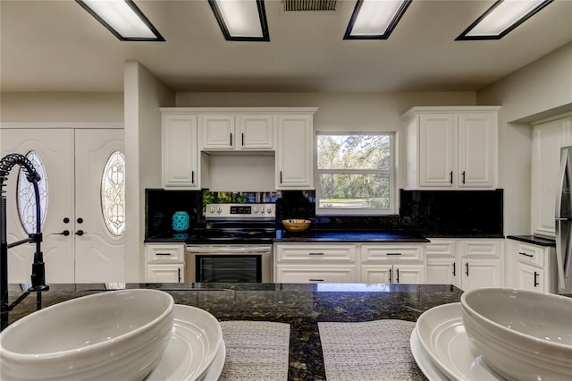 kitchen with dark stone counters, electric range, white cabinets, and decorative backsplash