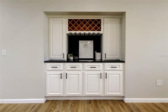 bar with light wood-type flooring and white cabinets