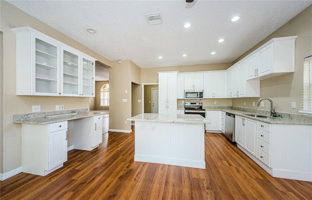 kitchen featuring sink, appliances with stainless steel finishes, a center island, light stone counters, and white cabinets