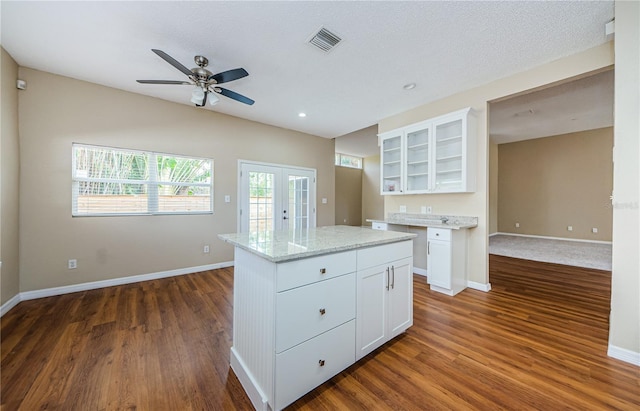 kitchen featuring a kitchen island, white cabinets, light stone counters, dark wood-type flooring, and french doors