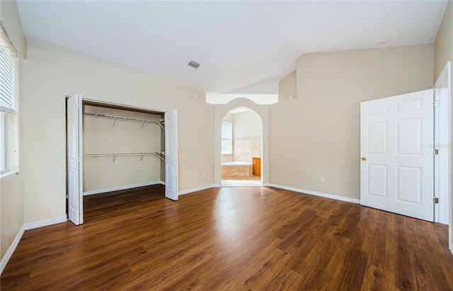 unfurnished bedroom featuring dark wood-type flooring, ensuite bathroom, vaulted ceiling, and a closet