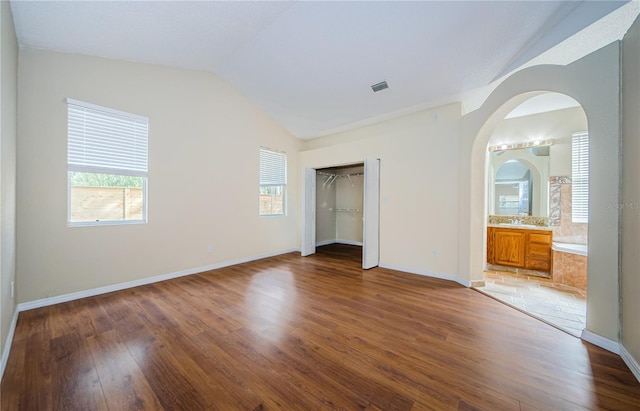 unfurnished bedroom with connected bathroom, wood-type flooring, lofted ceiling, sink, and a closet