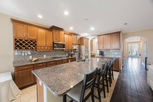 kitchen featuring light stone countertops, an island with sink, appliances with stainless steel finishes, and a breakfast bar