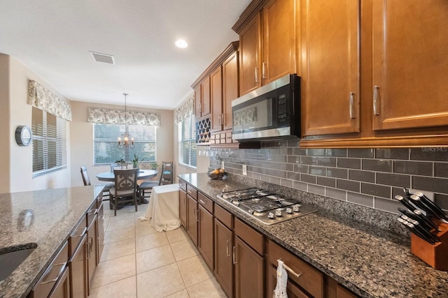 kitchen featuring light tile patterned flooring, dark stone counters, pendant lighting, stainless steel appliances, and backsplash