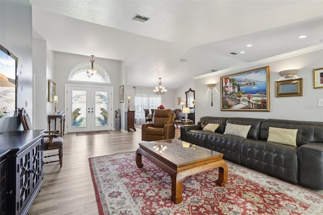 living room with french doors, a chandelier, vaulted ceiling, light wood-type flooring, and ornamental molding