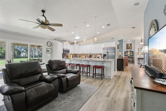 living room with vaulted ceiling, a textured ceiling, ceiling fan, and light wood-type flooring