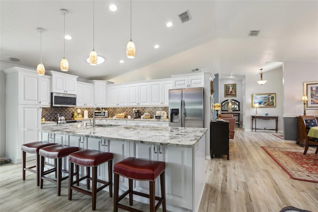 kitchen with sink, white cabinetry, hanging light fixtures, a large island with sink, and stainless steel appliances