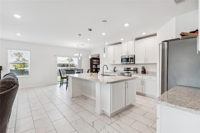 kitchen featuring sink, white cabinetry, stainless steel appliances, a center island with sink, and decorative light fixtures